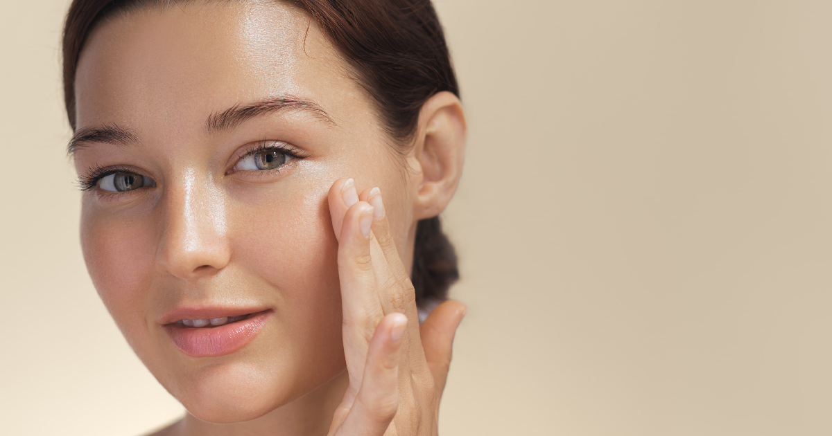 Young woman with radiant, glowing skin gently touching her face, showcasing a smooth and dewy complexion after a Korean Glass Skin Facial in Cary, NC